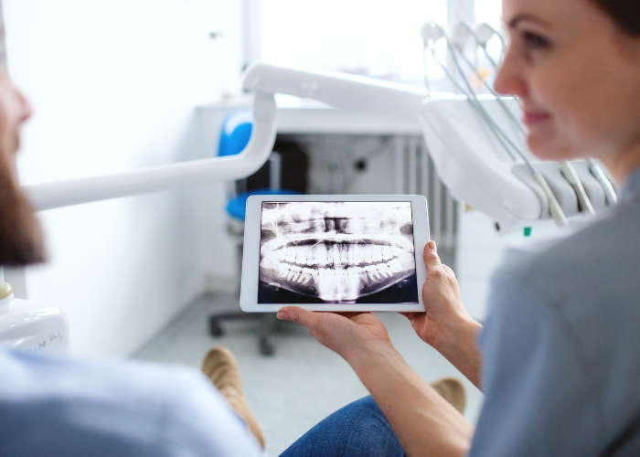 Patient and dental professional reviewing digital X-ray on tablet in modern dental office, showcasing advanced imaging technology for accurate diagnosis.